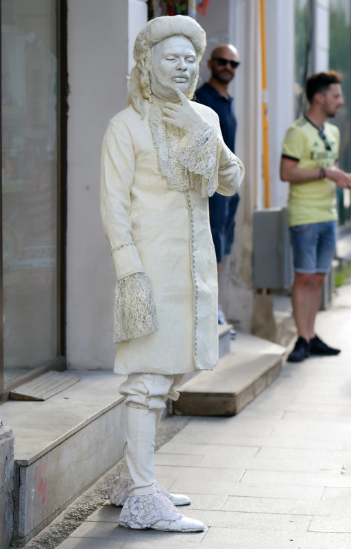 21 - A performer dressed as an 18th-century ghost or white living statue, posing in a public street
